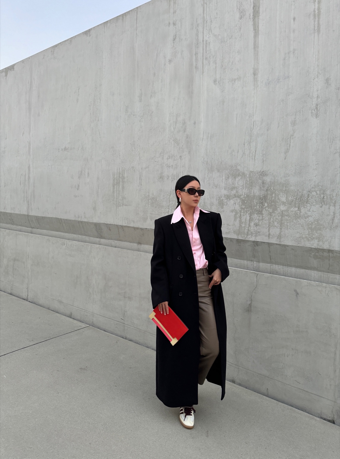 Black coat look with a red portfolio against a concrete wall